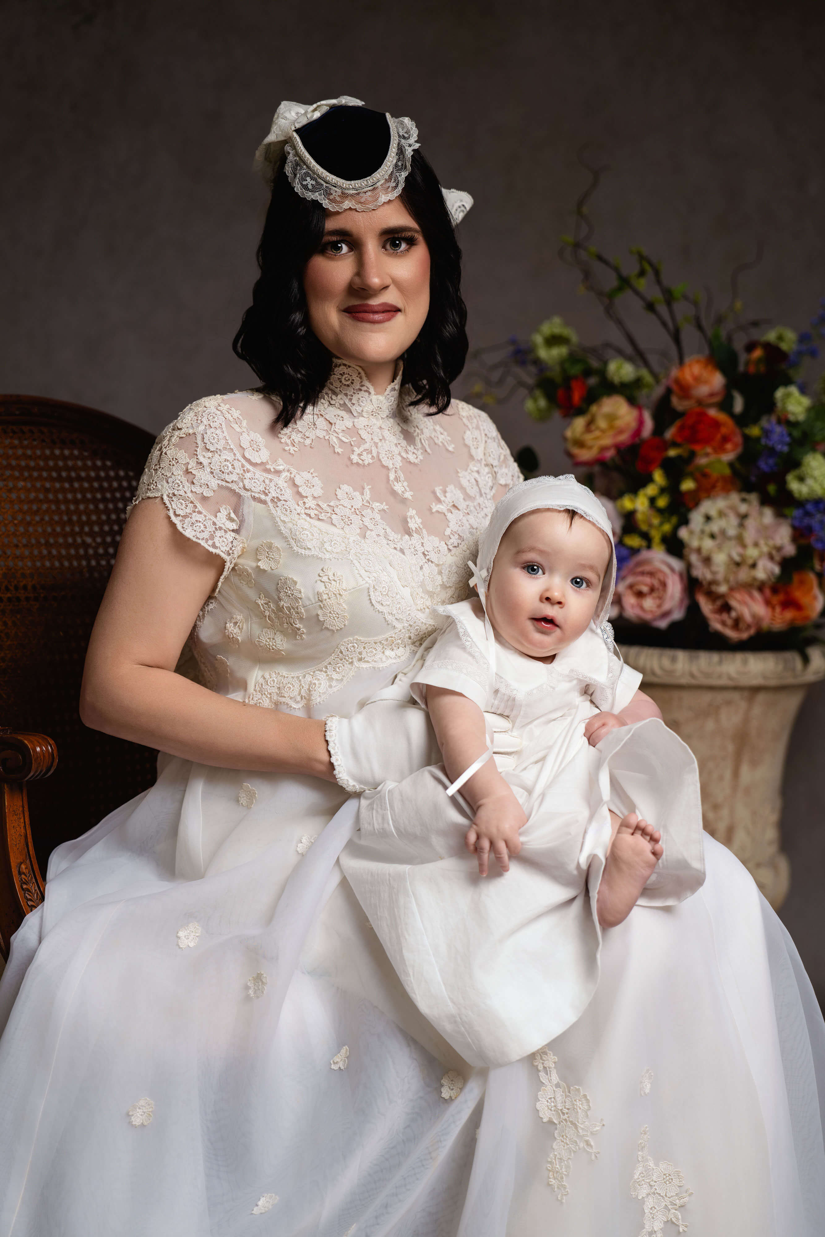 A mother and her baby in a beautiful wedding gown and christening gown and bonnet in a painterly family portrait created by Breanne Cook of Breanne Fine Portraiture in Birmingham, Alabama.